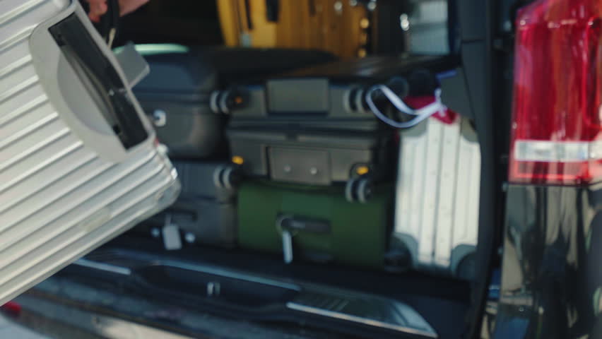 Person unloading suitcases in open van trunk, capacious automobile trunk full of baggage, preparation for departure on parking lot. High quality 4k footage