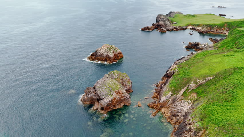 Green grass covering the rocks at the waterscape. Some bare boulders stick out form water. Aerial view.
