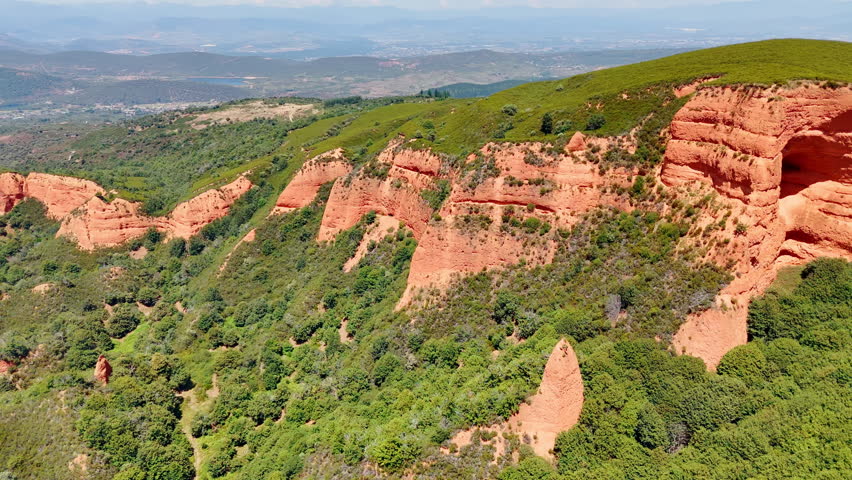 Orange rock formations with greenery on the slopes. Sunny view of the mountainous landscape from aerial view.