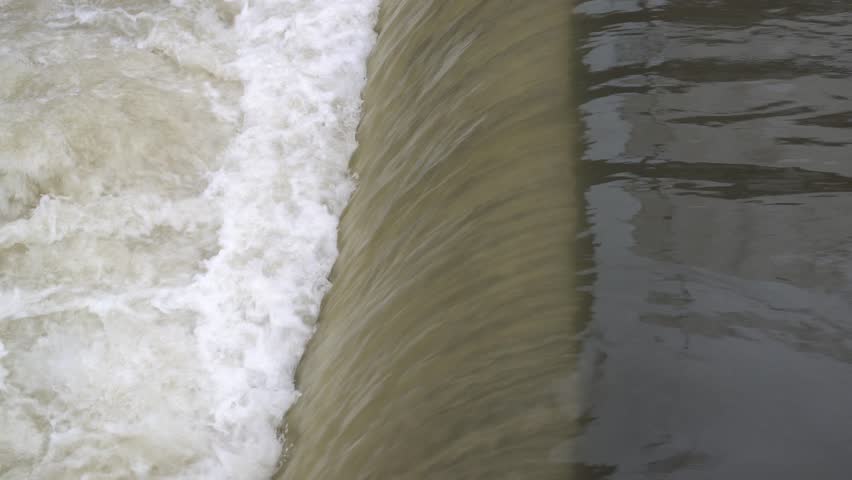 Industrial waterfall line Dam with foamy water flow closeup front side view, water flow from right to left.