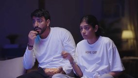 A husband and wife sit on the couch in the bedroom, focused on the TV as they enjoy a bowl of popcorn together. - Powered by Shutterstock - Get 15% off with code: PIKWIZARD15