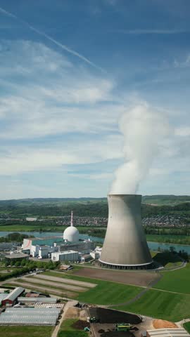 Working nuclear power plant in industrial zone against blue sky, Switzerland. Power station with working reactor with steam. Environmental conservation and energy production. Vertical video
