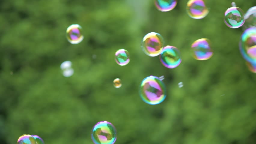 Colorful Large Soap Bubbles in Slow Motion. Holiday Background Birthday Close-up View of Beautiful Big Soap Bubbles is Flying Near Green Trees at Sunny Day. Party Bubbles Shimmering Colors of Rainbow.