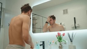 Shirtless man looks at himself in bathroom mirror. Man checking his wrinkles and hairs. Morning hygiene - Powered by Shutterstock - Get 15% off with code: PIKWIZARD15