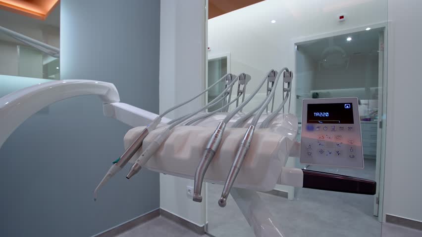 Close-up of dental instruments including handpieces, air scaler, and control panel with touch screen interface in clean and modern dental clinic with bright lighting and glass partitions