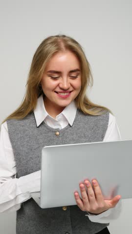 Young woman smiling while holding a laptop and wearing a stylish outfit indoors