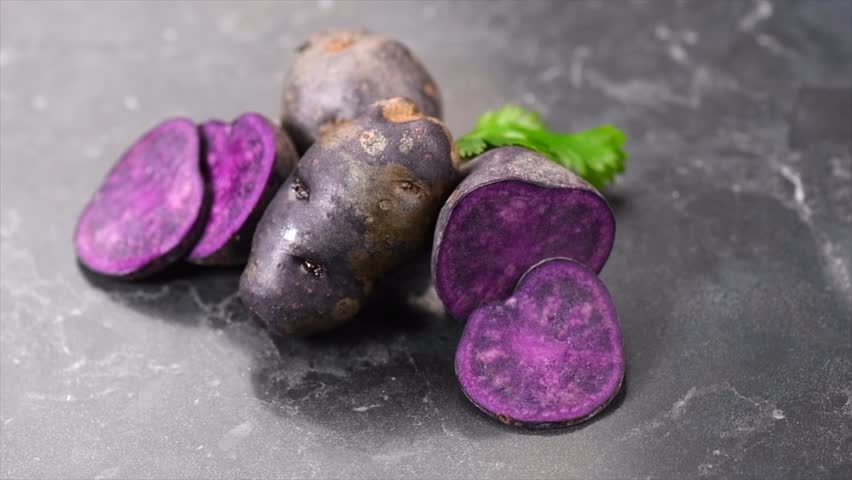Violet potato Vitelotte, blue-violet raw potatoes close-up. Purple organic homegrown potato on black table background. Healthy vegan food, delicatessen 