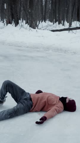Young man is skating on ice, his movements are unsteady, and he loses his balance, falling heavily onto slippery surface. He may have suffered a fracture or other injury.