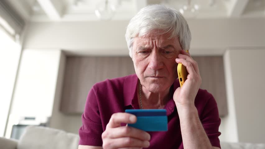 Trusting serious feared pensioner giving away card number to fraudsters over phone. Financial scam, identity theft, bank card fraud, information theft manipulation, deception, vulnerable individual