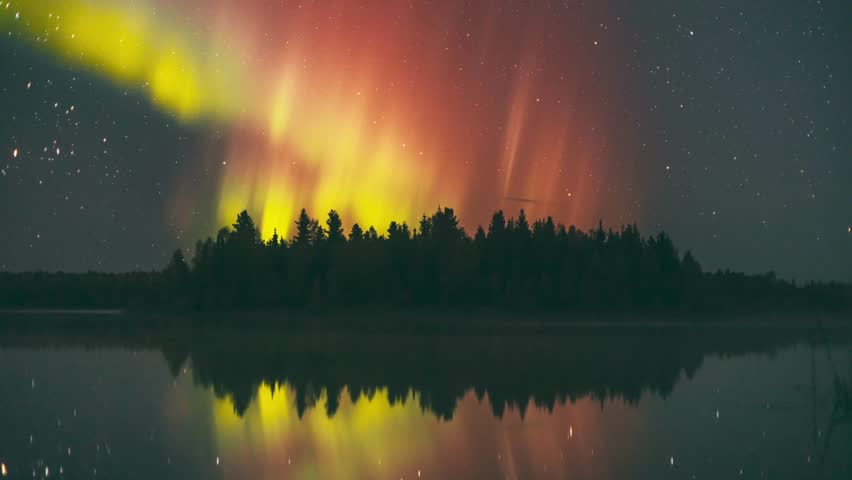 Time lapse shot of flickering yellow and red aurora borealis at night sky of Alaska, USA. Wide shot. Forest trees on Island with lake reflection of northern lights. Spectacular shot.