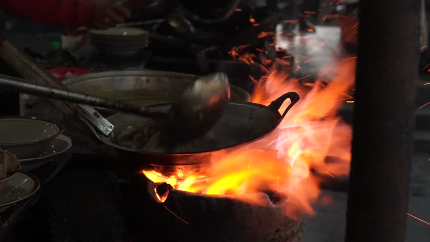 Cooking food on a stove with a lot of smoke and fire, live cooking in an open kitchen.
