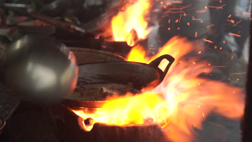 Cooking food on a stove with a lot of smoke and fire, live cooking in an open kitchen.