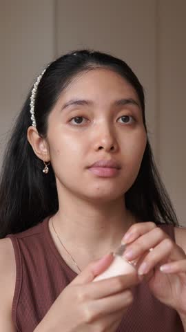 Focused young Asian woman pouring face cream foundation to her palm before applying make up complexion.