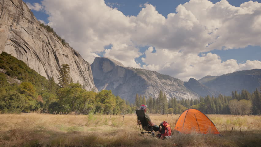 A picturesque camping scene in Yosemite National Park features a vibrant orange tent among majestic mountains, perfect for hiking enthusiasts and nature lovers eager to explore the outdoors