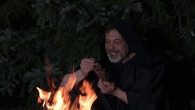 An elderly monk in a black robe counts money from his wallet while sitting by a fire at night in the woods - Powered by Shutterstock - Get 15% off with code: PIKWIZARD15