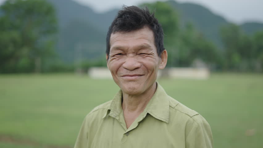 portrait of a mature Asian man farmer with lots of wrinkles on his face smiling and waving at the camera in Vietnam