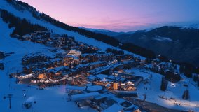 Aerial view of Courchevel, France, at night, featuring a winter landscape with glowing lights, snow-covered peaks, ski slopes, chalets, and a luxury resort in the French Alps, with gently falling snow - Powered by Shutterstock - Get 15% off with code: PIKWIZARD15