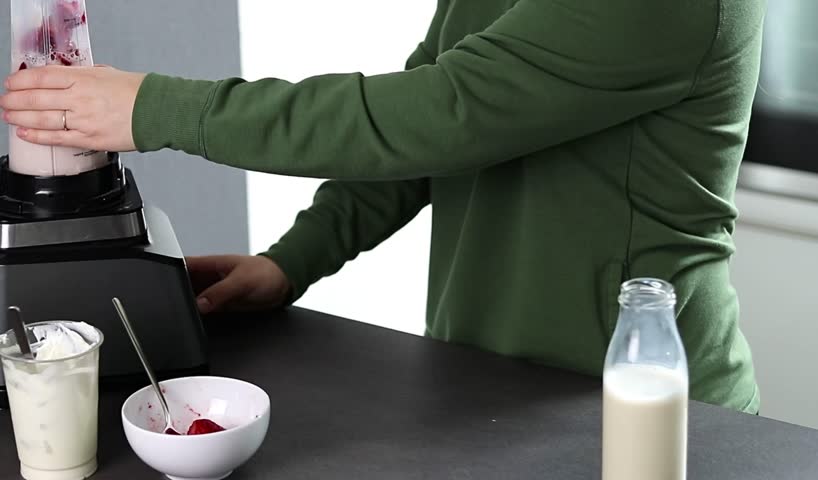 Close up of a woman in green sweater preparing fresh strawberries smoothie with yogurt and milk in the kitchen 