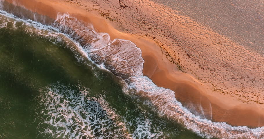 Aerial view of foamy waves reaching sandy coastline near Varna, Bulgaria. Sunlight casts golden glow textured beach, contrasting deep green ocean smooth shore in perfect natural harmony. Meditation