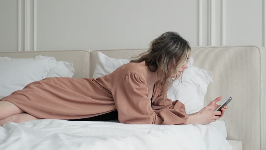 Portrait of a beautiful young woman using a phone while lying in bed