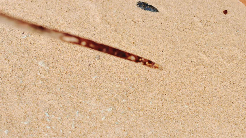 A stick traces a triangle shape in the warm, fine-grained sand of a beach - 4K