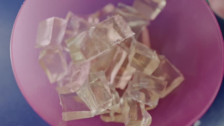 A detailed view showcasing translucent gelatin cubes in varying shades, housed elegantly in a soft pink bowl. Close-Up of Shimmering Gelatin Cubes in a Pink Bowl