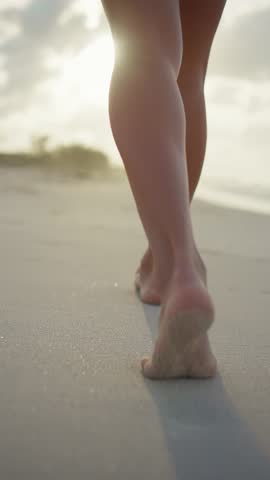 Barefoot woman walking on beautiful sandy beach, leaving footprints on sand, back view on slender legs. Female sexuality and tenderness of lady body, rest in paradise, summer vacation on seashore