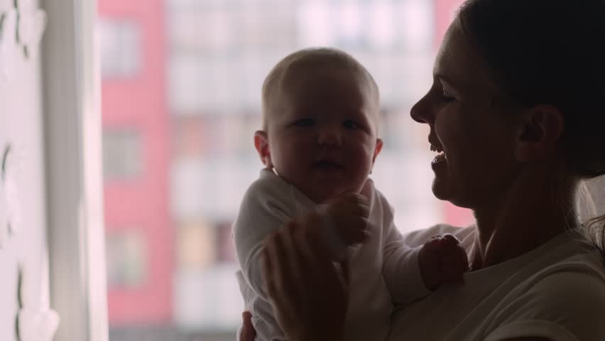 silhouette parent mother lifts baby into the air near window, creating a beautiful silhouette against soft curtains, expressing joy and excitement, family love, bonding, childhood happines