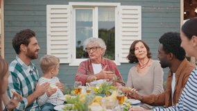 Big family sitting together at table. People listening to grandfather talking. Explaining something to relatives. Thanking everyone for coming and visiting them at village. House in background. - Powered by Shutterstock - Get 15% off with code: PIKWIZARD15