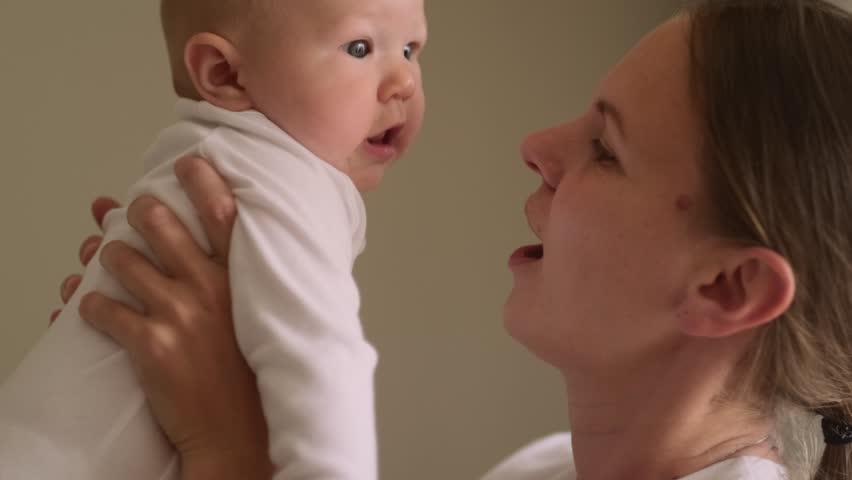 mother and baby share joyful moment as they smile at each other, baby is held securely in the mother arms, looking at her with delight, family love, bonding, parenting, childhood happines