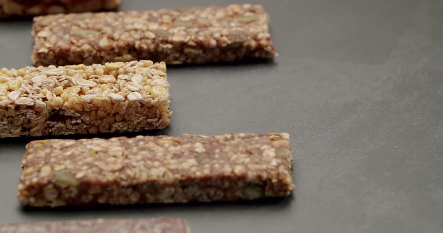 Close-up shot of various granola and protein bars on a dark surface. Ideal for fitness, health, and snack-related concepts. Assorted Healthy Granola And Protein Bars Arranged On Dark Background
