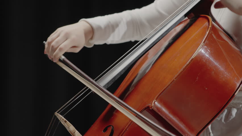 A beautiful woman sitting and playing the cello in a studio on a black background. Classical music playing stringed classical musical instruments, Closeup view of violoncello and hands of musician