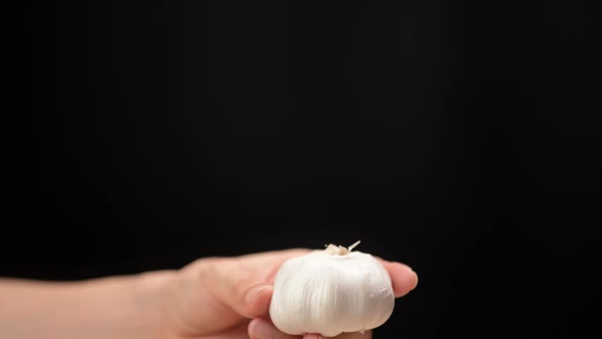 Hand holding fresh garlic clove kitchen counter food dark background close-up perspective culinary ingredient