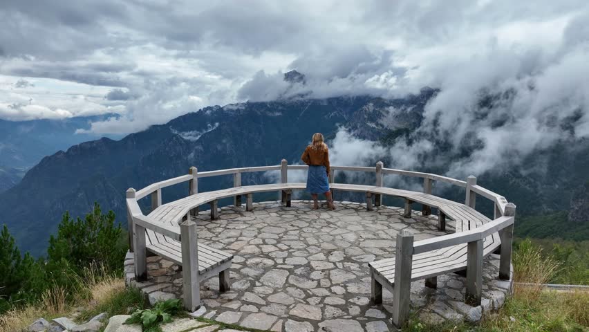 Aerial orbit of woman looking out across scenic mountain vista viewpoint in Theth, Albania, admiring rugged peaks and deep valleys