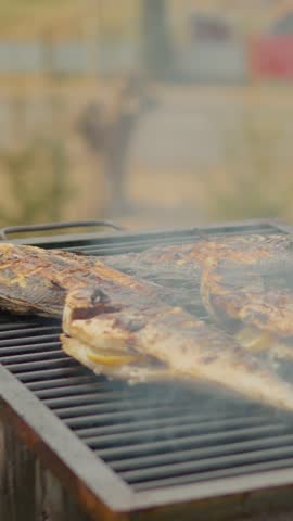 Vertical Screen: Sea bream with lemon on barbecue sizzling on barbecue grill, golden surface glistening with lemon slices, cheese, chef carefully seasoning delicate fillet