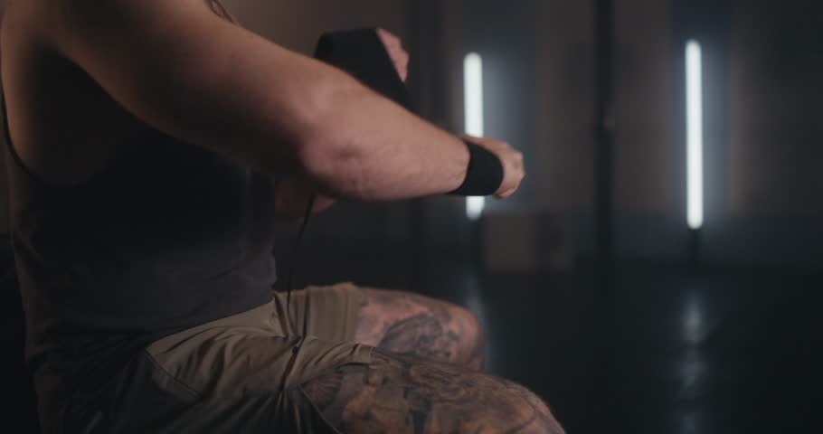 Close-up of a muscular man tightening wrist wraps before workout in a dimly lit gym