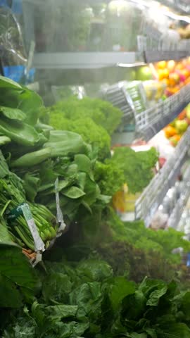 Vertical screen, spinach bunches receiving light water misting while resting in refrigerated supermarket produce display case