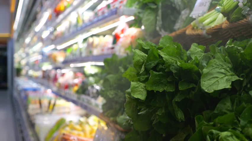 Refrigerated grocery store display maintaining green vegetable freshness through fine water vapor misting, preserving moisture and preventing leafy greens dehydration. Greens on store shelves