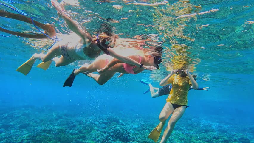 Group of female tourists snorkels in the tropical water. Young woman looking in camera and showing sign of heart. Bali. Indonesia