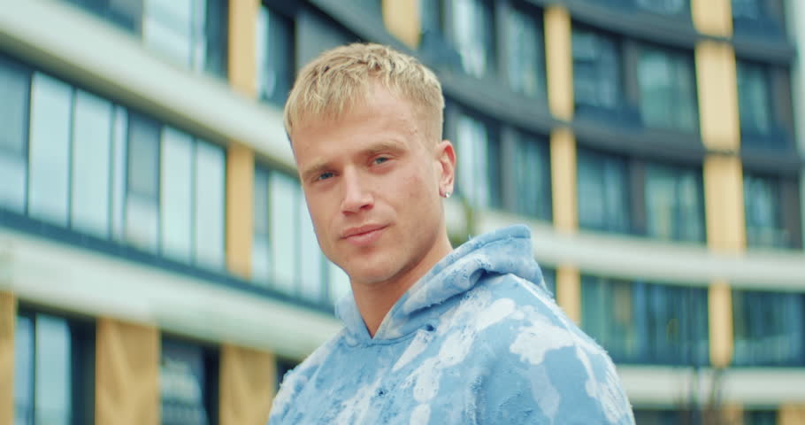 Stylish young man in a trendy blue tie-dye sweatshirt turns to the camera and smiles