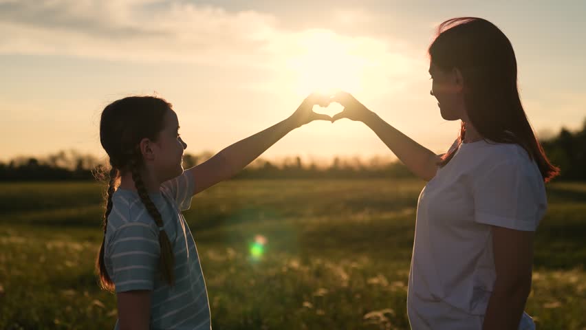 Heart-shaped hands at sunset by daughter and mother, Beautiful sunset with heart hands by mom and girl, Mother and daughter love symbol with hands at sunset, Sunset connection with mother and daughter