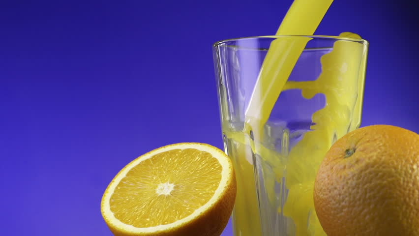 Orange juice pouring in glass on color background
