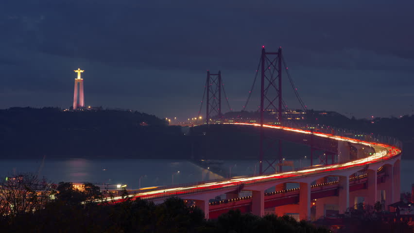 Bridge from Miradouro do Bairro do Alvito tourist viewpoint with Tagus river, traffic on 25th of April Bridge in the dark against the backdrop of a statue of Christ. Lisbon, Portugal. Timelapse