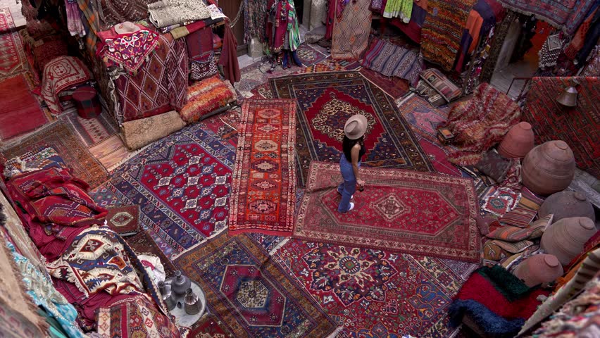 A photographer tourist browses handmade carpets and kilims in a shop, capturing the intricate designs with a camera. Authentic carpets hang wall, reflecting the rich culture of Cappadocia, Turkey.
