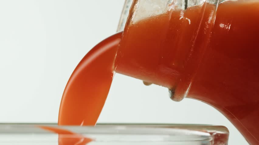 Woman pouring carrot juice from jug into glass at wooden table, closeup