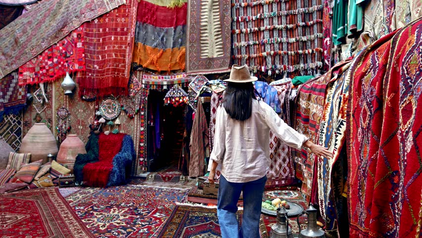 A photographer tourist browses handmade carpets and kilims in a shop, capturing the intricate designs with a camera. Authentic carpets hang wall, reflecting the rich culture of Cappadocia, Turkey.