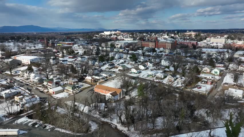 Row of houses in small american town during snowy winter day. Aerial forward wide shot. Sunny day with clouds at sky. Downtown buildings and blocks in background. Lynchburg, Virginia, USA.
