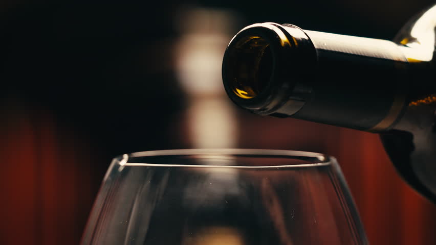 Orange or red wine bottle and glass against a sunset in a peaceful vineyard, pouring of ecological natural wine. 