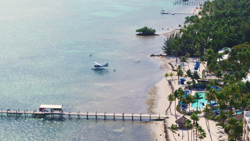 This stunning aerial image beautifully showcases the captivating coastline and vibrant, lush scenery of Key West, Florida, with tranquil waters, tropical greenery, and a seaplane docked on the water.