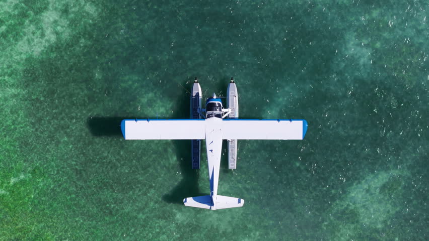 This aerial shot captures a seaplane docked on crystal-clear waters in Key West, Florida, as the camera ascends, revealing vibrant tropical colors and the scenic beauty of this coastal paradise.
